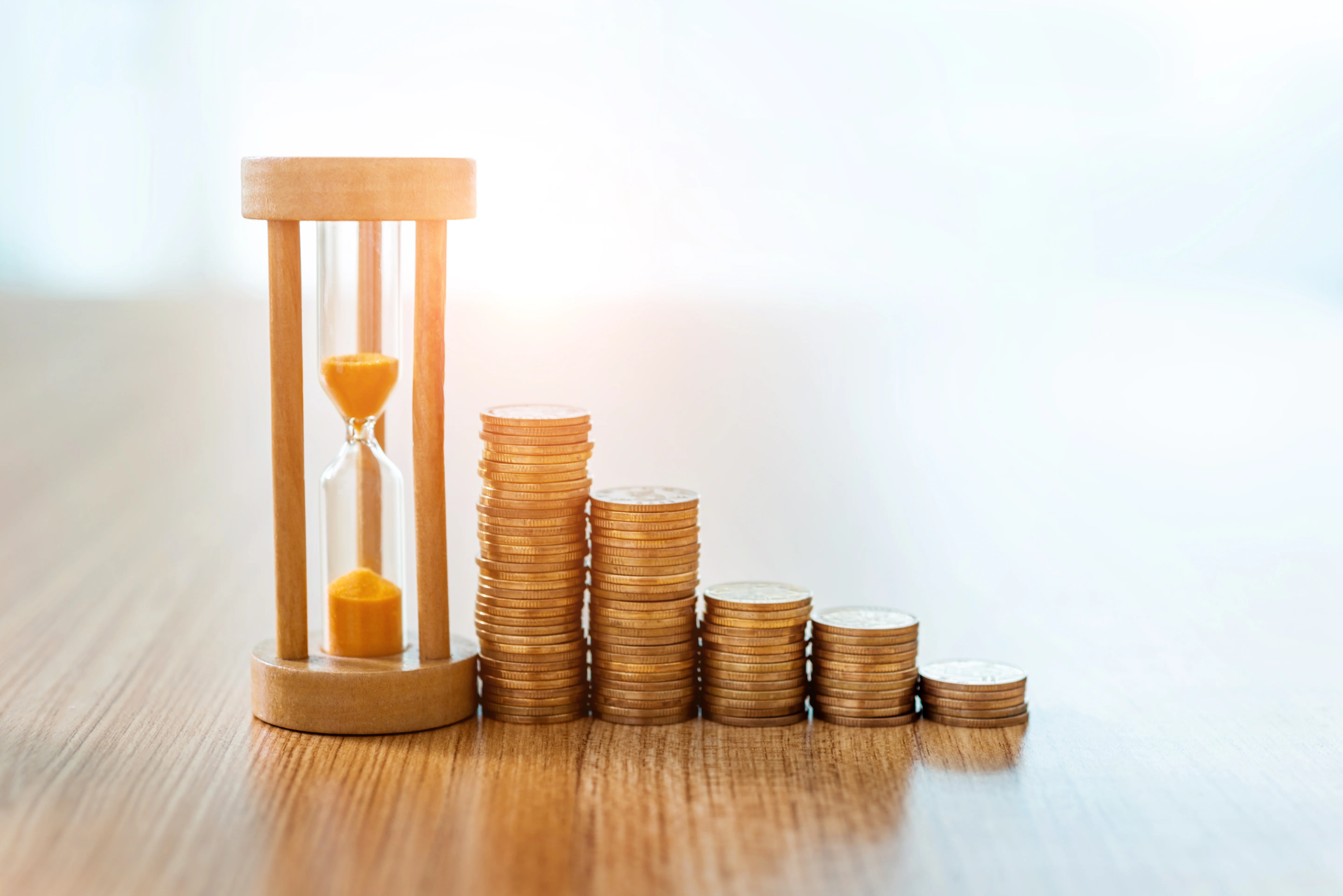 An hourglass and coins on a wooden table.