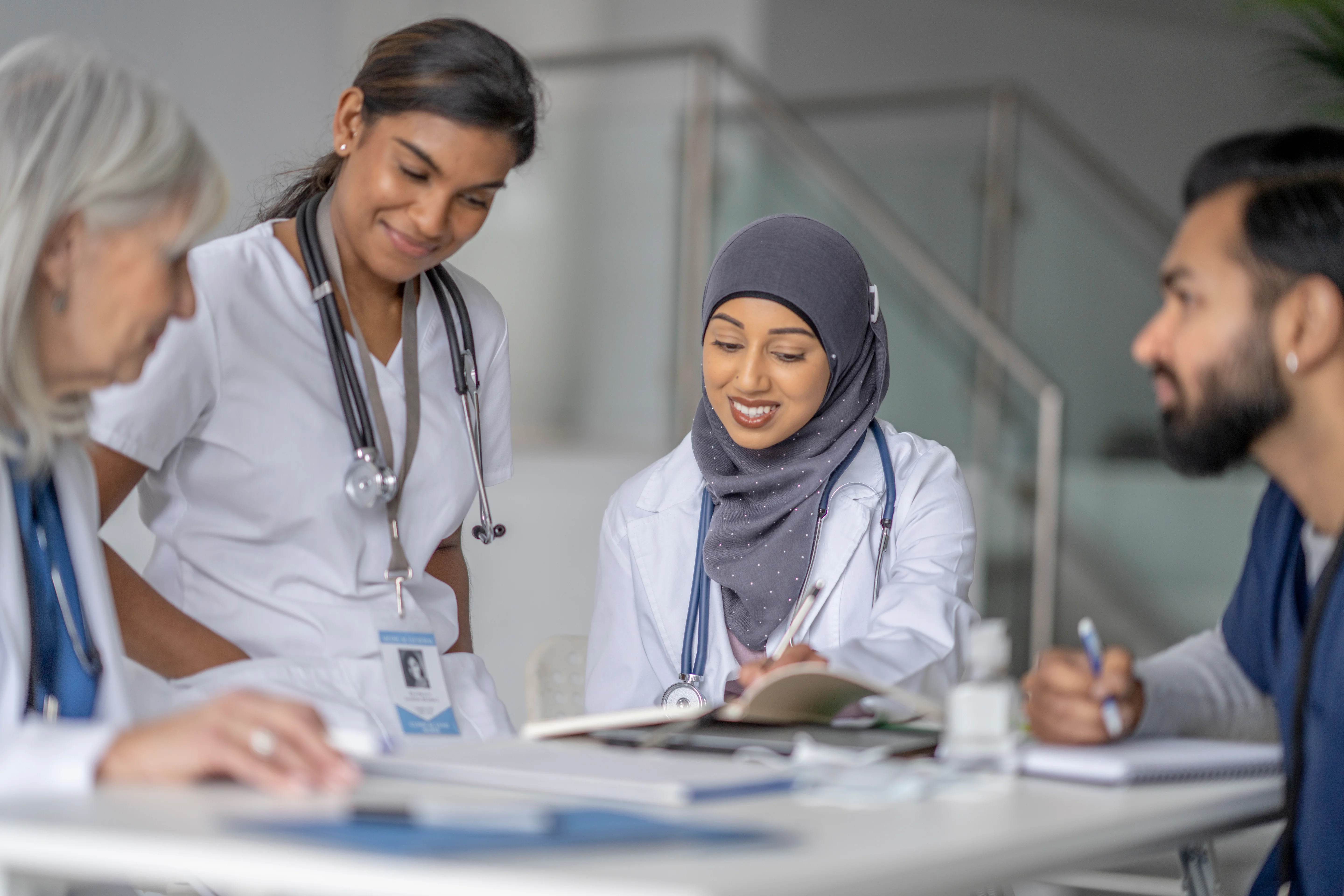 A small group of three medical students sit around a table as they meet with their teacher to review patient cases.